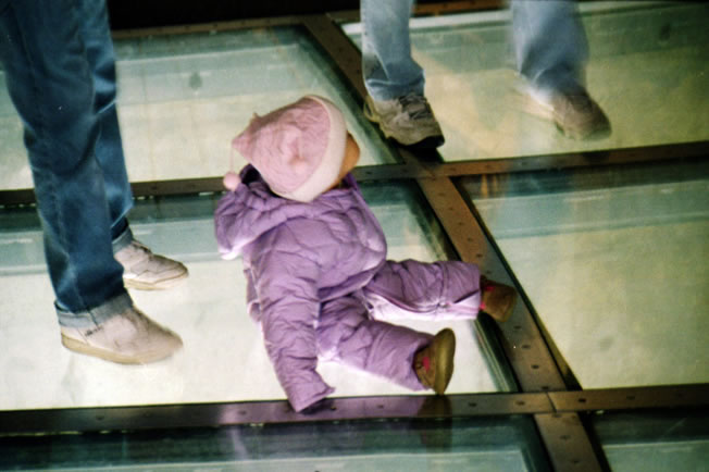 A child is sitting on the glass segments in the floor of the visitor level of the CN tower
