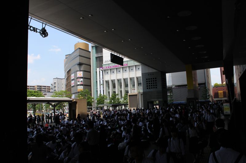 Große Anzahl an Schülern wartet geduldig auf dem Boden hockend im Bahnhof Kyoto Station