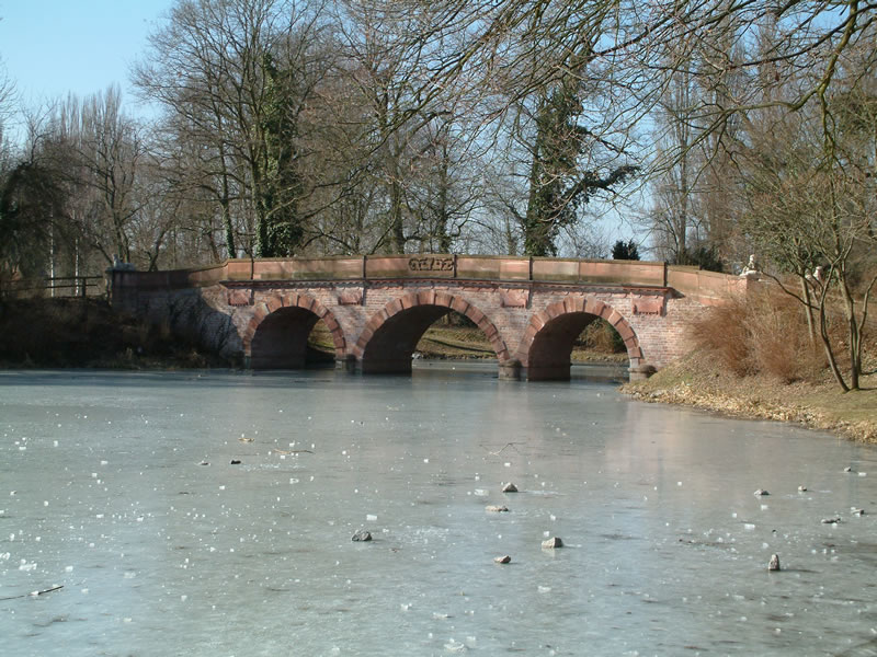 Park Schönbusch in Aschaffenburg. Der See ist komplett zugefroren. Über dem Eis erhebt sich die Brücke der alten Landstraße nach Darmstadt.