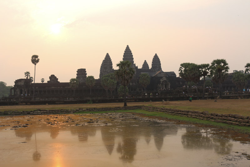 Blick über den (reichlich verschlammten) Spiegelsee zu den Haupttempeln von Angkor Wat während des Sonnenuntergangs und Gegenlicht.