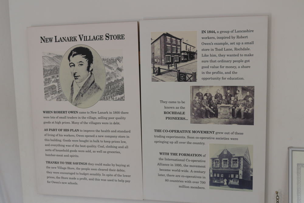 Informationstafel, die auf Englisch einige Hintergrundinformationen zur Funktion und Arbeitsweise des New Lanark Dorfladens liefert.