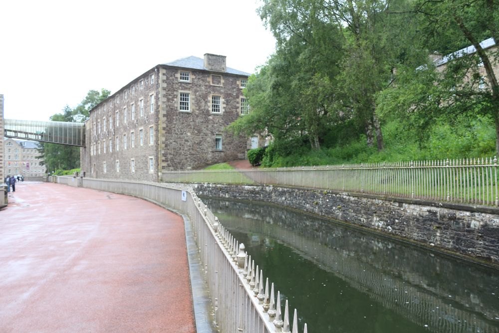 The water canal delivers water from an elevated point above the close by rapids to the big wheels. The height difference between the canal and the river provides the necessary energy to propel the water wheels and the machinery in the factory.
