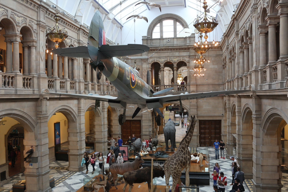 West Court hall of Kelvingrove Museum with a Spitfire LA198 hanging above an elephant, a giraffe, etc.