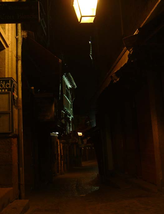 Auf dem dunklen Bild wirkt die Altstadt von Mont-Saint-Michel beinahe gruselig. Vereinzelte Lampen durchbrechen die Schatten der engen Straße.