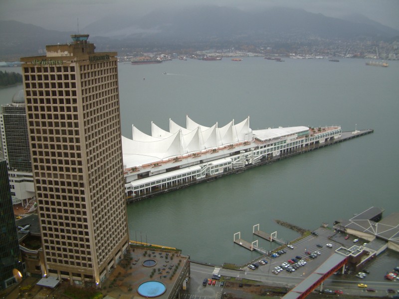 Blick von der Aussichtsplattform "Vancouver Lookout!" auf dem Dach des Harbour Centre Tower über das Konferenzzentrum Canada Place. Dieses Gebäude dient auch als Anlegestelle für große Kreuzfahrtschiffe.

Links das dunkelbraune Gebäude der Zeitung Sun Province. Auf dem Dach befindet sich der Kontrollturm der Flugüberwachung. Von dort wird der rege Flugverkehr mit Wasserflugzeugen im Hafengebiet gesteuert.