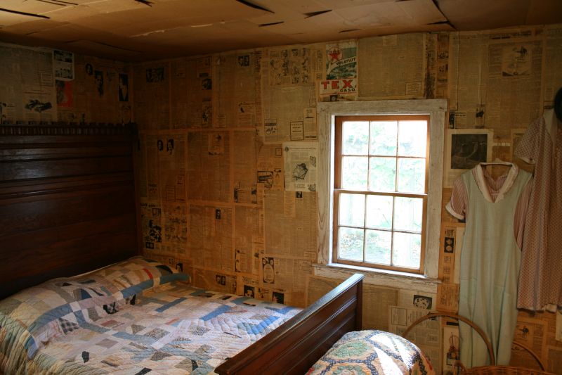 Schlafzimmer& im Haus der Mattox Familie. Das Gebäude ist ein Beispiel für die Lebensbedingungen ärmerer Menschen während der Großen Depression. Die Wände sind mit Zeitungen aus der Zeit tapeziert.