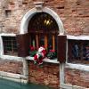 Santa Claus sits on a window sill above one of the canals of Venice