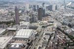 Blick aus einem Hubschrauber über Frankfurt am Main: Die Frankfurter Messe mit dem auffälligen silbernen Dach der Halle 3. Dahinter das bunte Skyline Plaza Shopping Center. Der große bleistiftartige Wolkenkratzer in der Mitte ist der Messeturm. Davor versteckt sich die große Frankfurter Festhalle. Auf der rechten Seite befinden sich der Hauptbahnhof sowie der Fluss Main, der sich durch die Stadt schlängelt.